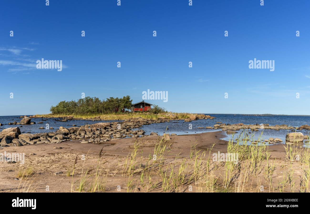 Un pintoresco paisaje costero en el Mar Báltico con una pequeña casa de campo roja en una isla detrás de una playa de arena bajo un cielo azul Foto de stock