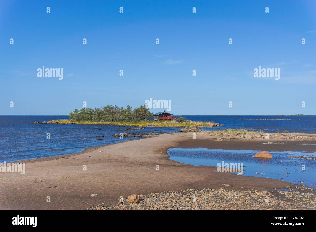 Un pintoresco paisaje costero en el Mar Báltico con una pequeña casa de campo roja en una isla detrás de una playa de arena bajo un cielo azul Foto de stock