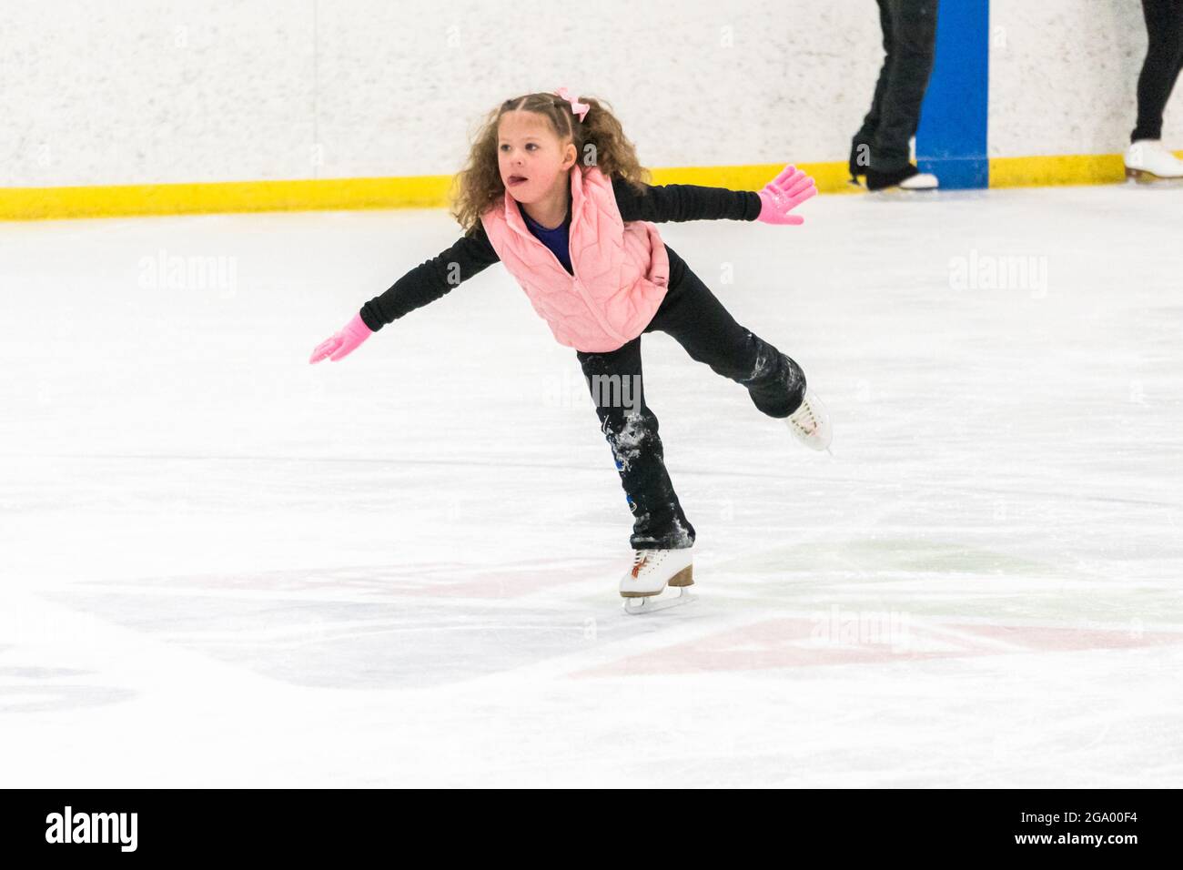 Niña practicando patinaje artístico en una pista de hielo cubierta.