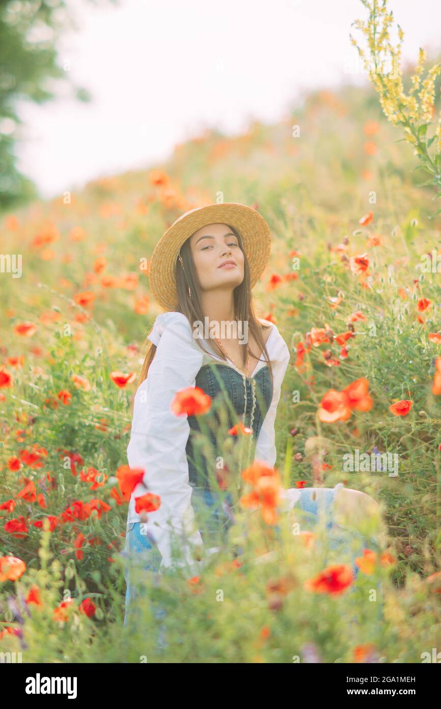 Mujer joven en sombrero de paja goza por la floración amapolas entre prado. Foto de stock