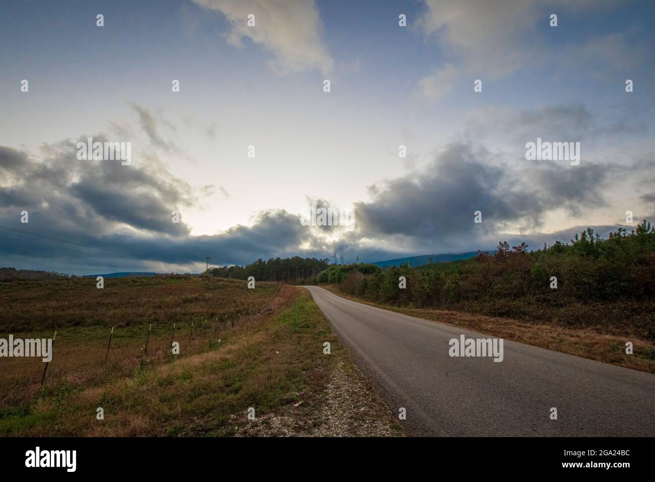 Imagen de fondo de un camino rural vacío que conduce a la distancia con luz que se desvanece detrás de grandes nubes. Foto de stock