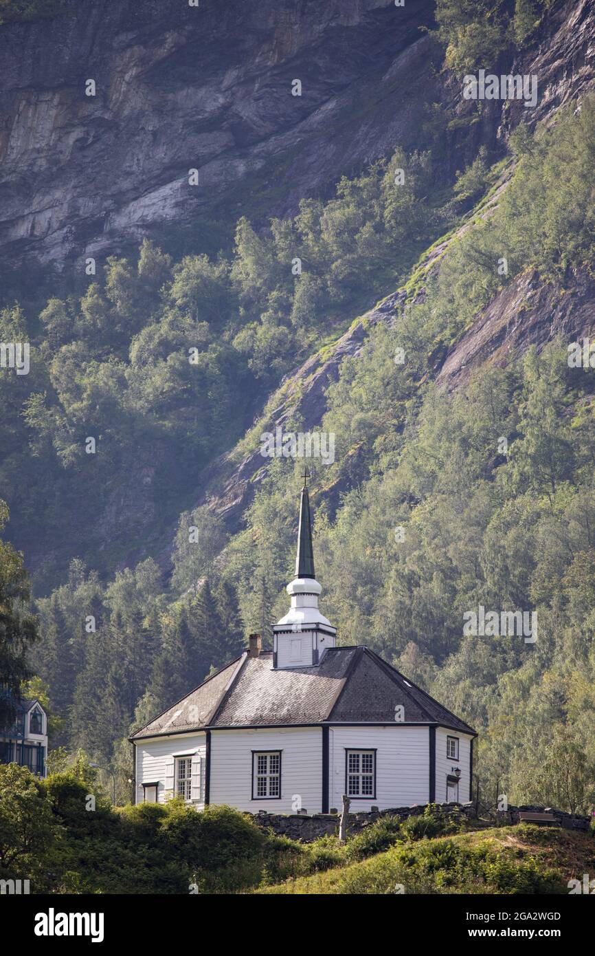 Una iglesia con campanario al lado de una montaña en Geiranger, Noruega; Geiranger, Sanda, Noruega Foto de stock