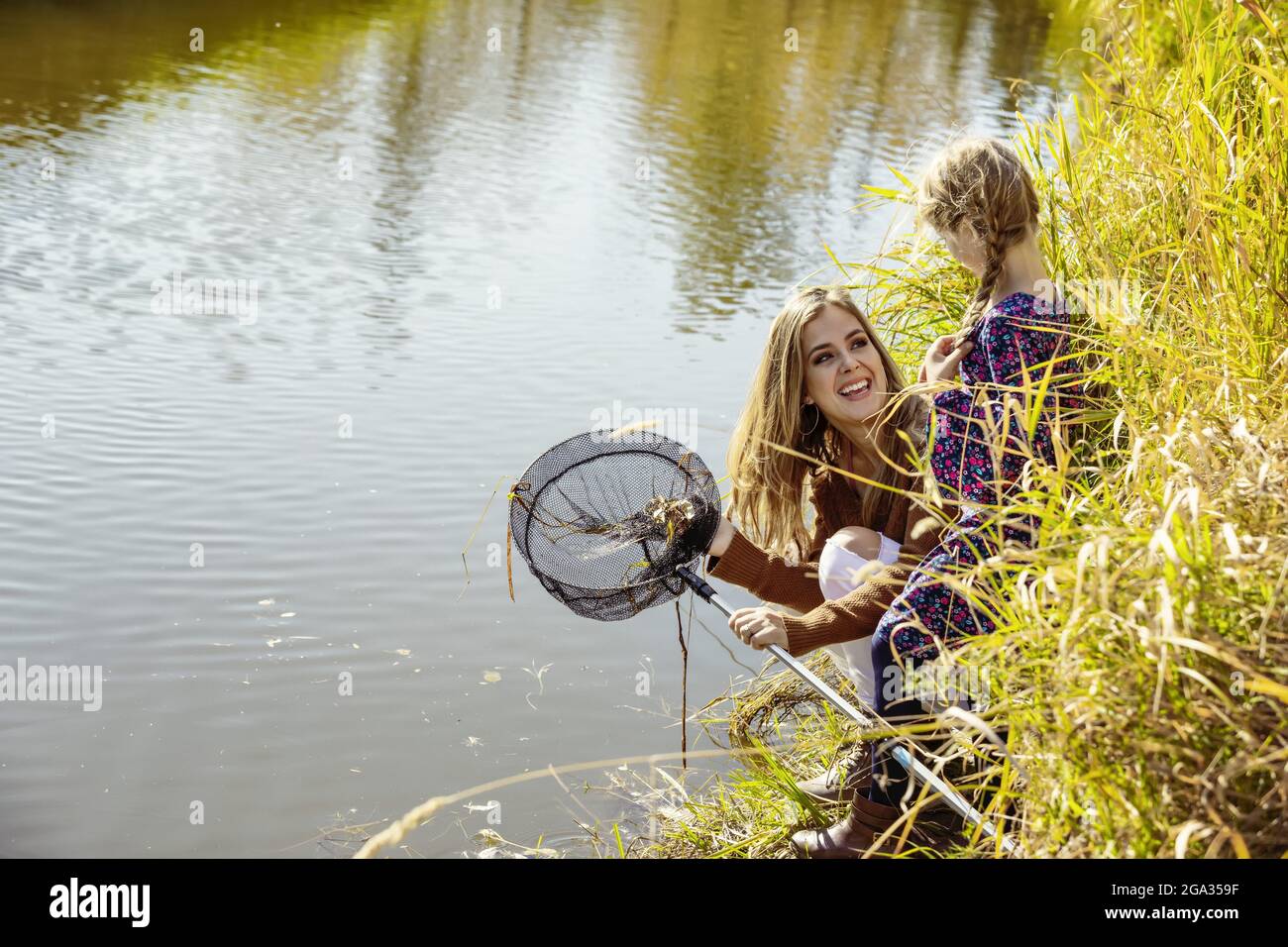 Una madre pasa tiempo de calidad al aire libre con su hija y utiliza una red para atrapar insectos en un arroyo en un parque de la ciudad; Edmonton, Alberta, Canadá Foto de stock