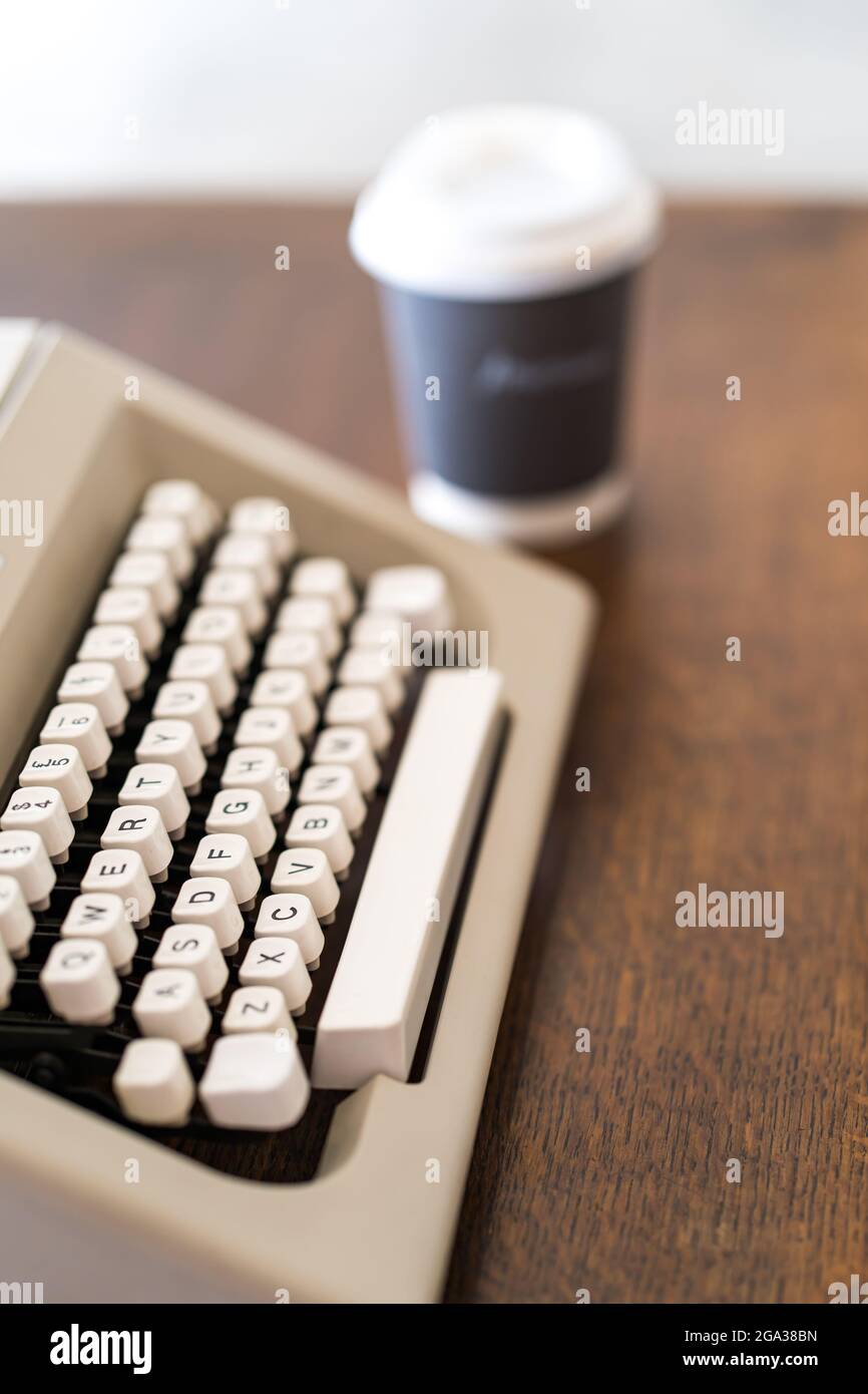 Disparo vertical de una máquina de escribir vintage junto a una taza de café de papel Foto de stock