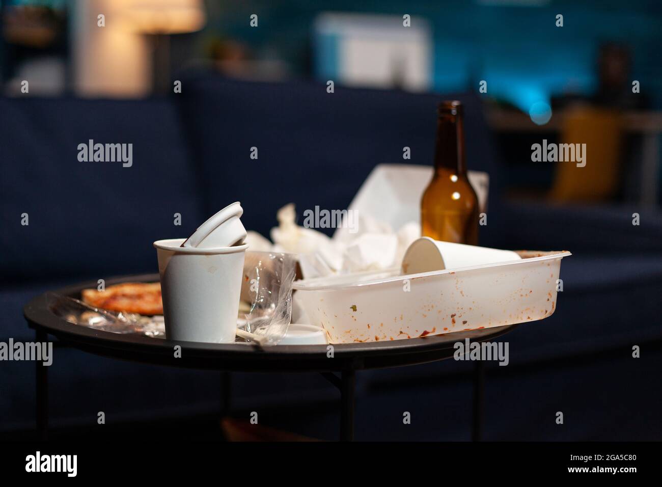 Basura en el salón vacío con basura de comida, botella de alcohol y servilletas en el sofá azul. Apartamento de la casa de la miseria de la mujer solitaria con la depresión mental que tiene la miseria, la basura sin ninguna gente adentro Foto de stock