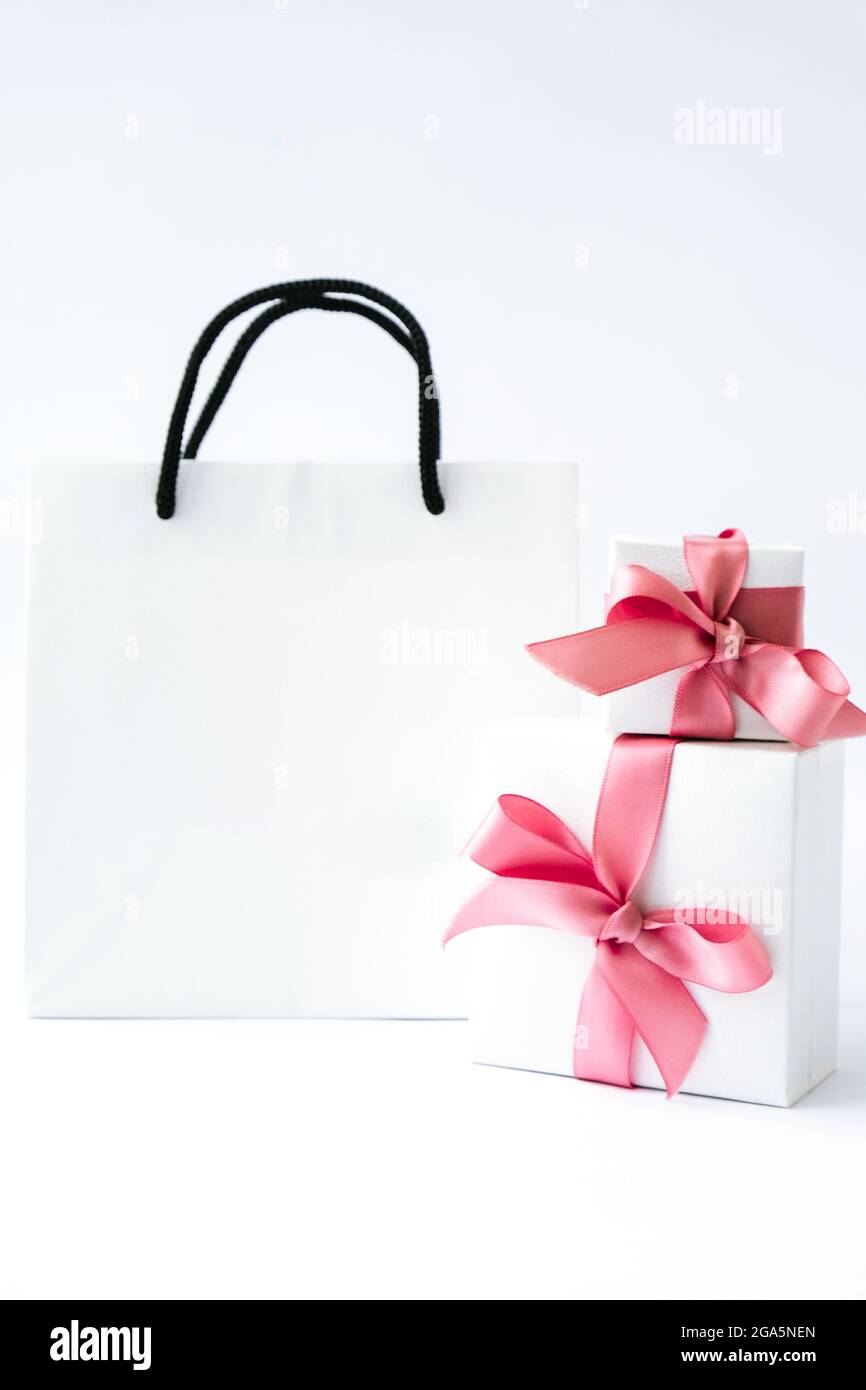 Bolsa blanca de papel en blanco y dos cajas regalo con cinta rosa sobre  fondo blanco. Rebajas de black friday. Concepto de compras. Burlamiento de  la compra de papel b Fotografía de