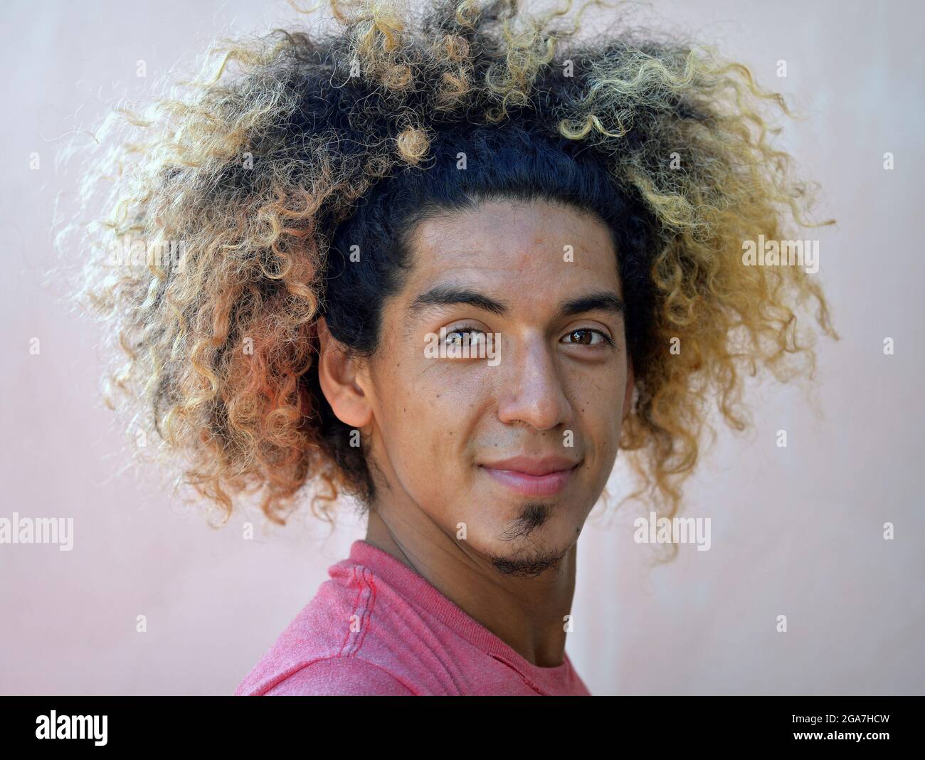 El joven latinoamericano con un choque de pelo rizado salvaje y cabello  teñido rubio termina sonriendo con la boca cerrada en la cámara Fotografía  de stock - Alamy
