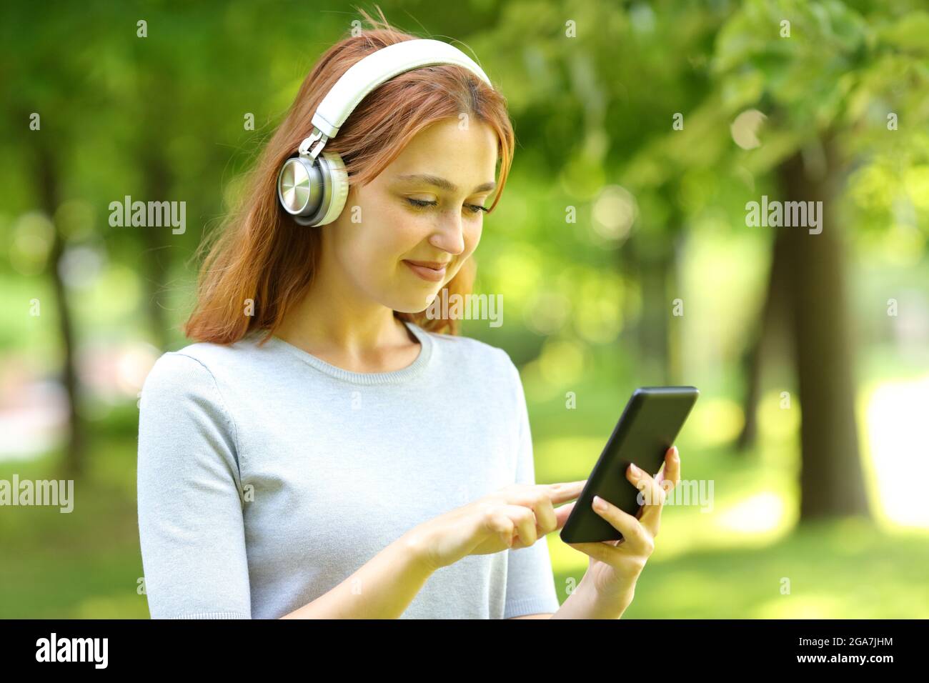 Mujer satisfecha con auriculares comprobando música en un teléfono inteligente en un parque Foto de stock