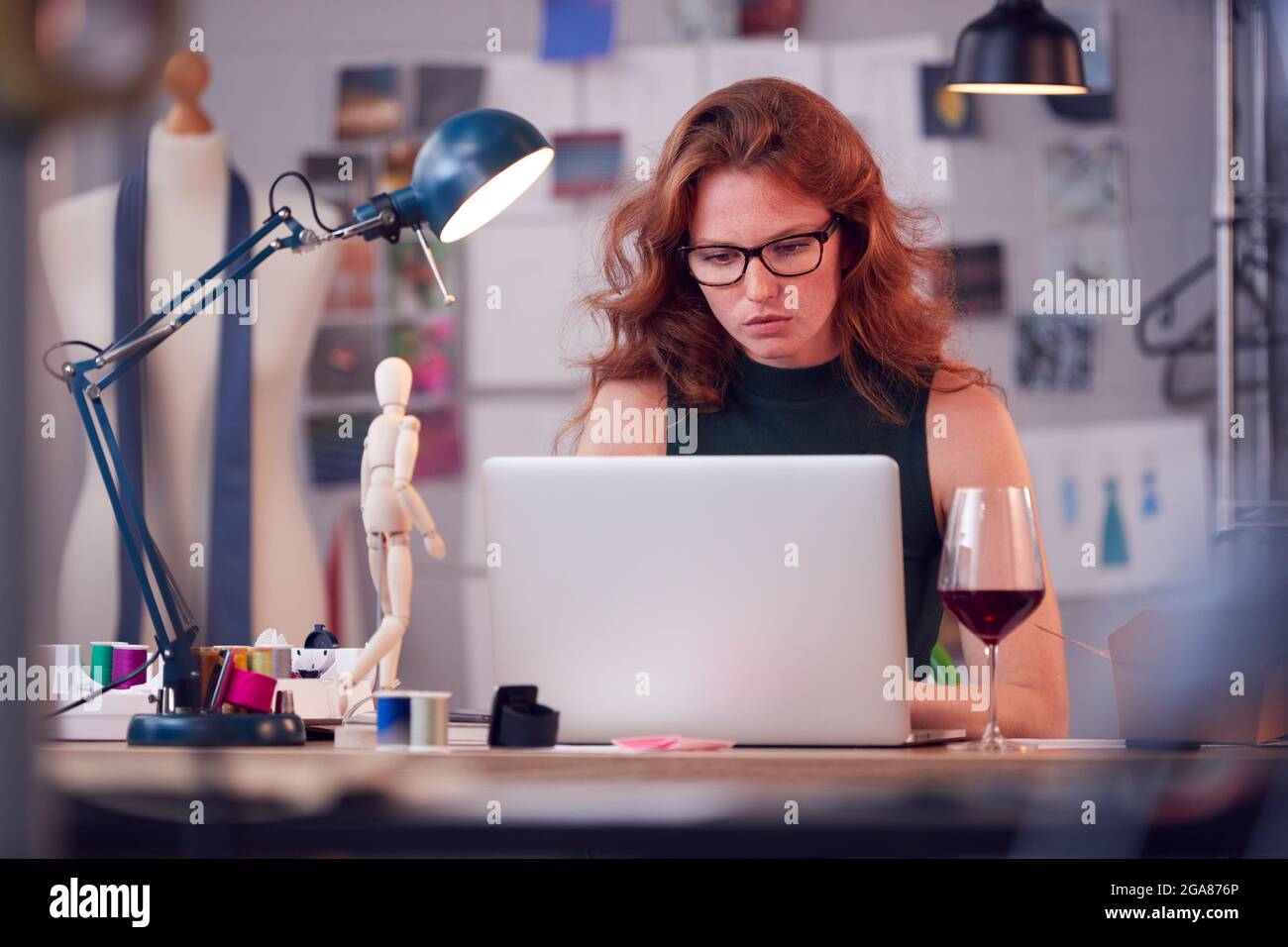 Mujer Dueño de Negocios de Moda con Copa de Vino Trabajando tarde en el portátil en el estudio Foto de stock
