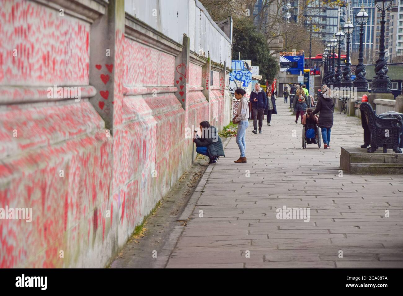 Londres, Reino Unido. 13th de abril de 2021. La gente añade corazones rojos en el National COVID Memorial Wall fuera del St Thomas' Hospital. 150.000 corazones rojos han sido pintados por voluntarios y miembros del público, uno por cada vida perdida por COVID-19 en el Reino Unido hasta la fecha. Foto de stock