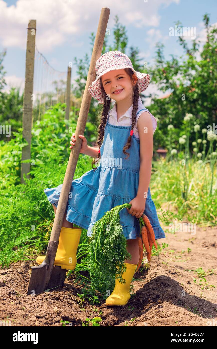 Un niño pequeño y hermoso con zanahorias en el jardín. Niña campesina, horticultura. Foto de stock