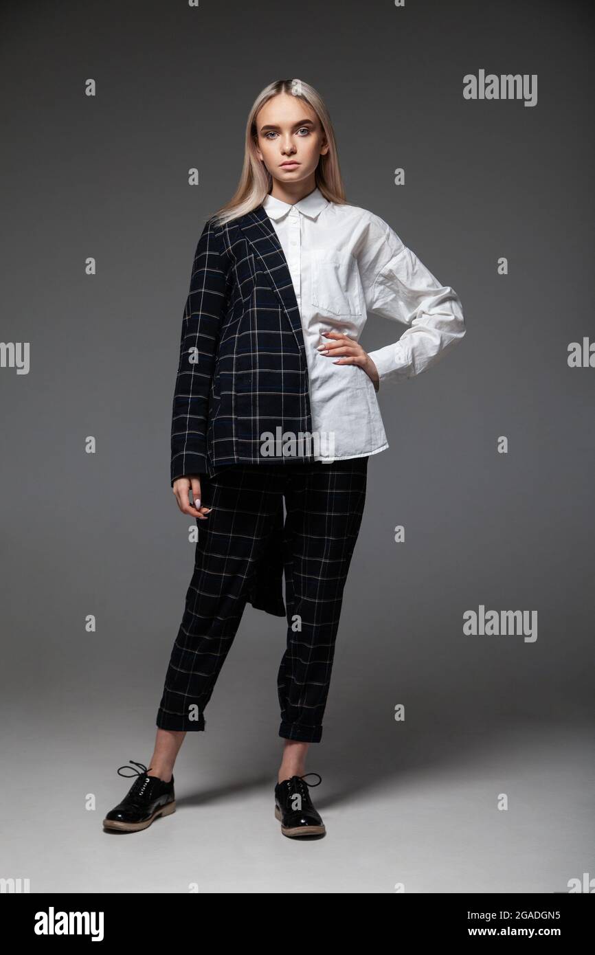 Modelo de mujer joven de cuerpo entero con ropa moderna y elegante que toca la cabeza y se inclina atrás sobre un fondo gris Fotografía de stock - Alamy