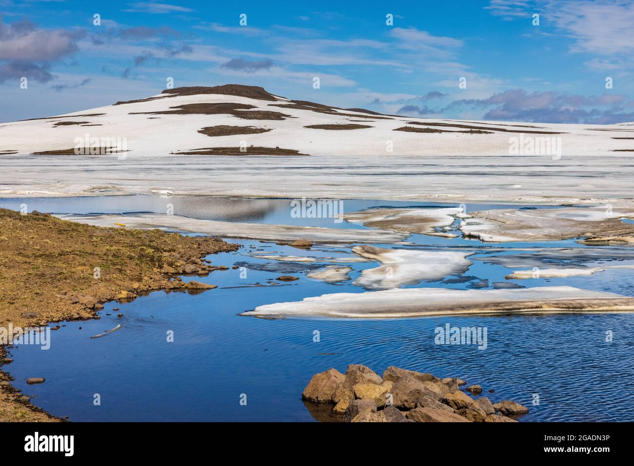 vista espectacular de las colinas volcánicas nevadas y negras reflejadas en las tranquilas piscinas azules en el camino al ferry de seydisfjordur Foto de stock