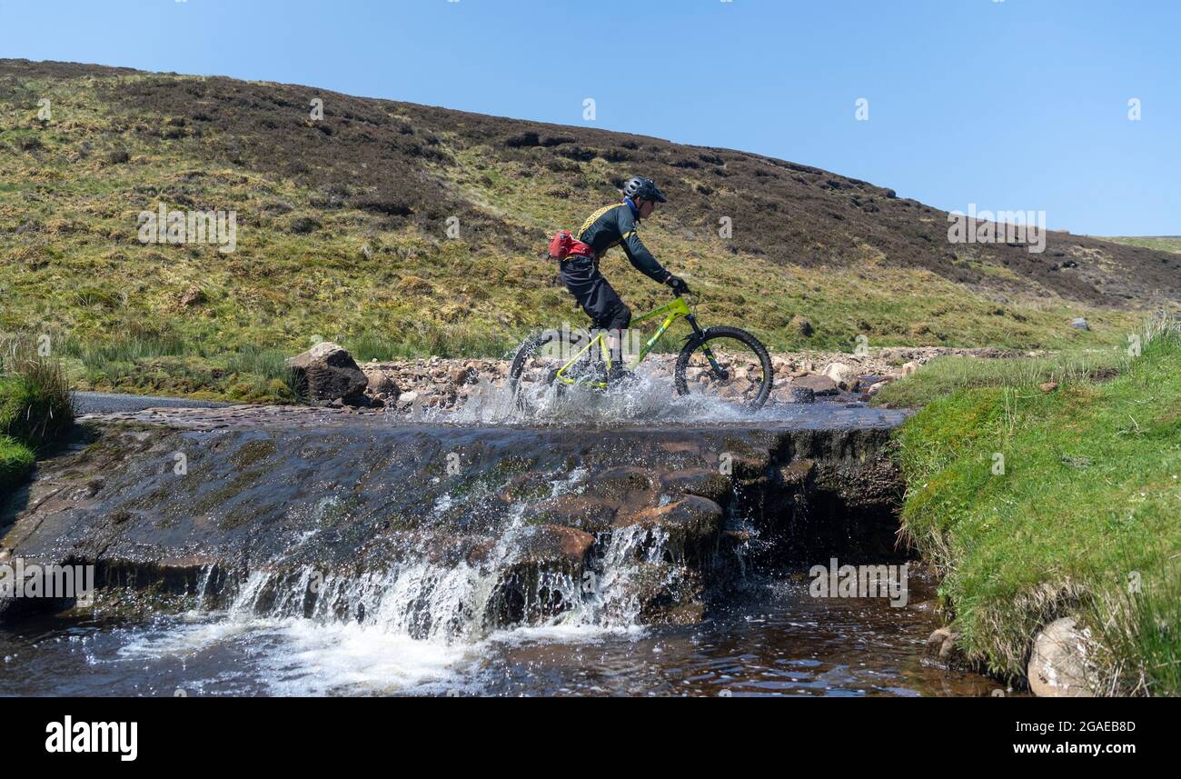 Ciclistas de montaña en Yorkshire Dales pasando por un arroyo cerca de Reeth, North Yorkshire, Reino Unido. Foto de stock