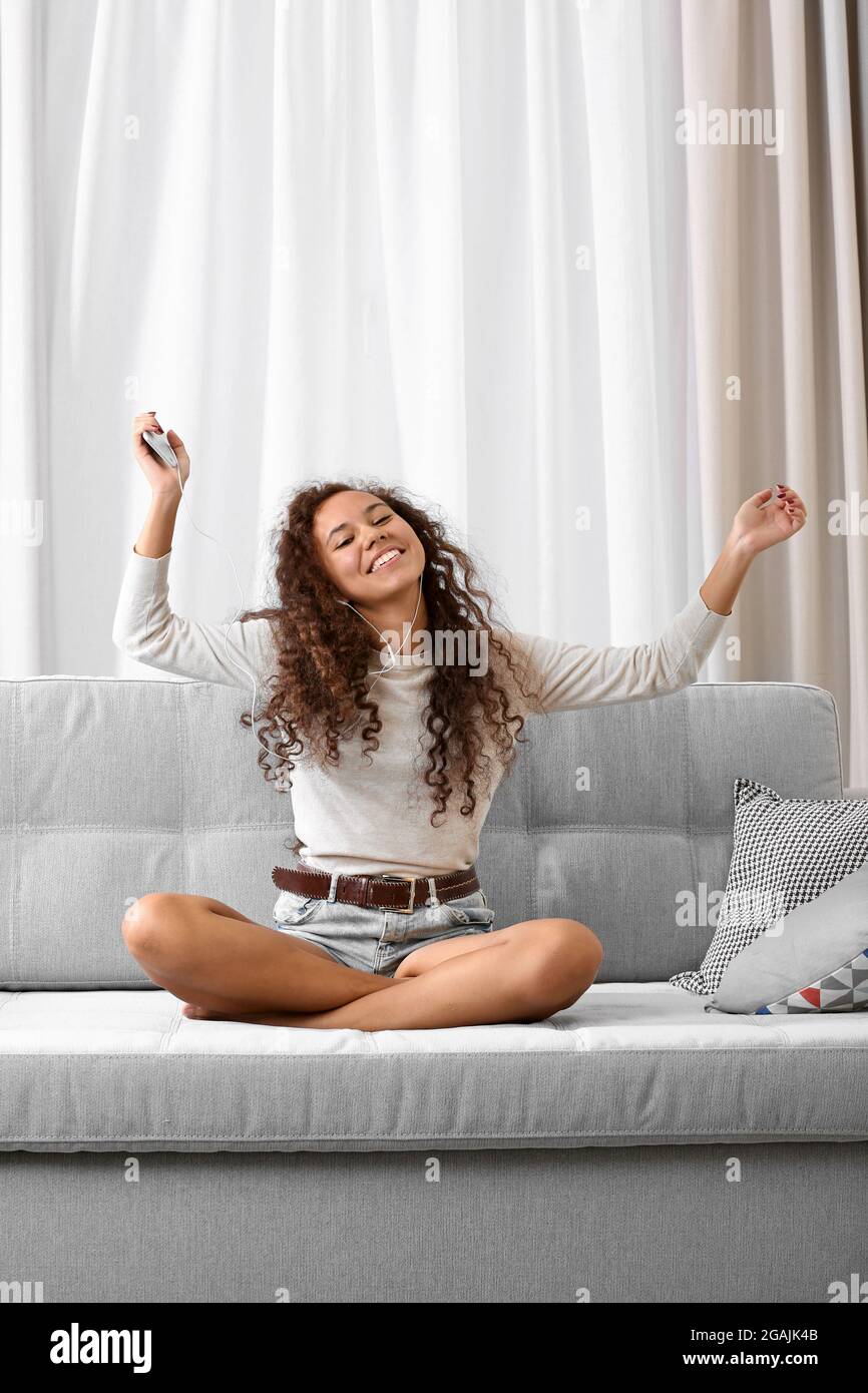 Hermosa niña escuchando música con auriculares y cantando canciones en un sofá  en la habitación Fotografía de stock - Alamy