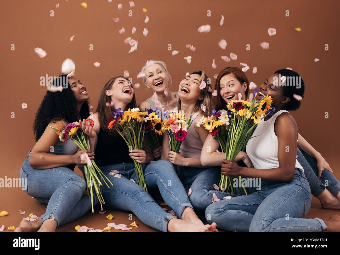 Grupo de mujeres diversas con ramos que se divierten bajo pétalos que caen.  Seis mujeres felices sentadas juntas sobre un fondo marrón Fotografía de  stock - Alamy