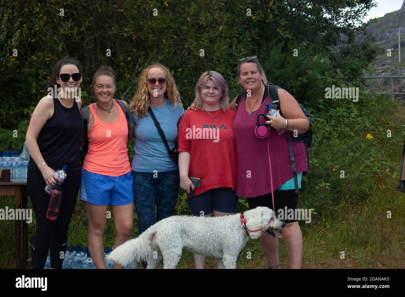 SAT 31 Jul 2021 Adrigole, West Cork Irlanda. Familia y Amigos de la víctima de un accidente trágico Tadgh Murphy realizó una caminata conmemorativa en ayuda de la ambulancia aérea de respuesta rápida de la comunidad irlandesa. Tagdh, de 19 años, murió después de que el coche en el que viajaba entrara en el río en la carretera Glengarriff-Kenmare junto con otro hombre, Michael Bowen (40) en las primeras horas del lunes 2 Otros hombres sobrevivieron al accidente. Los participantes de la caminata se ponen de pie con la hermana de Tadgh Tracey y Rosie el perro. Crédito ED/Alamy Live News Foto de stock