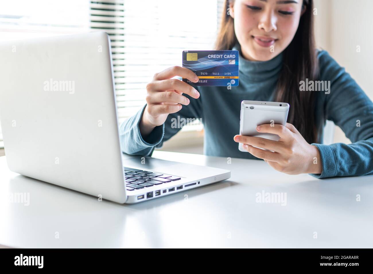 Asia hermosa mujer buscando número en la tarjeta de crédito para pagar el teléfono blanco para comprar en línea Foto de stock