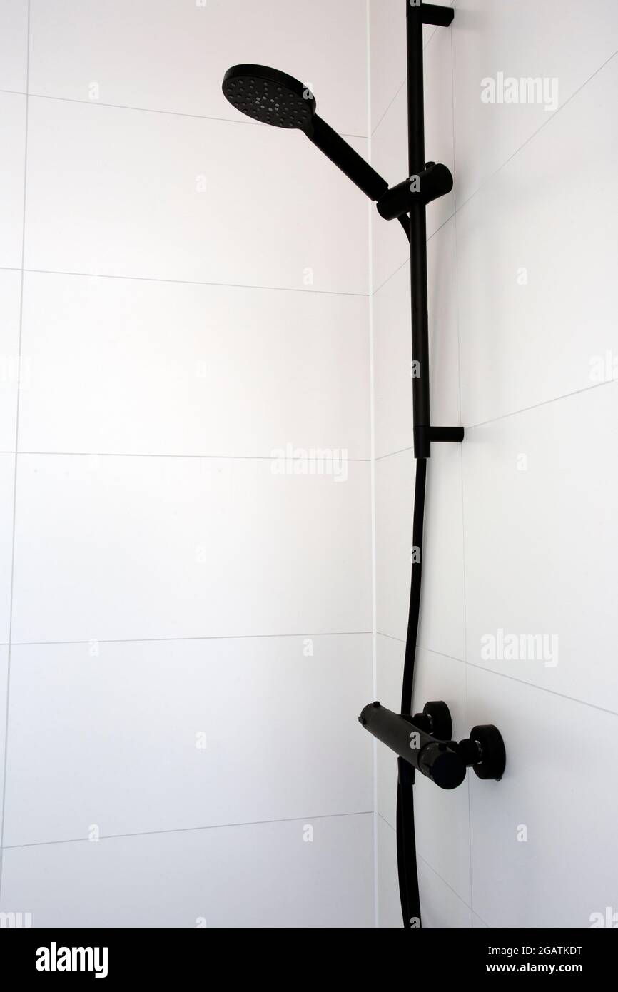 Cerca de la moderna y elegante alcachofa de ducha negra y el baño con  azulejos casi blancos en un moderno apartamento. Nuevo cabezal de ducha  negro en el soporte contra azulejos limpios