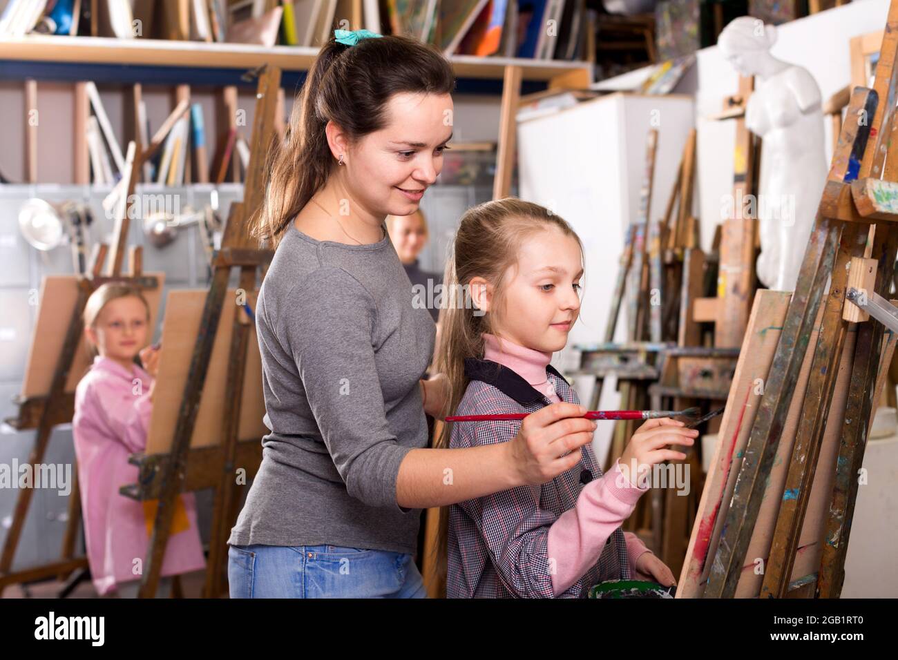 Maestra que ayuda a la niña durante la clase de pintura Foto de stock