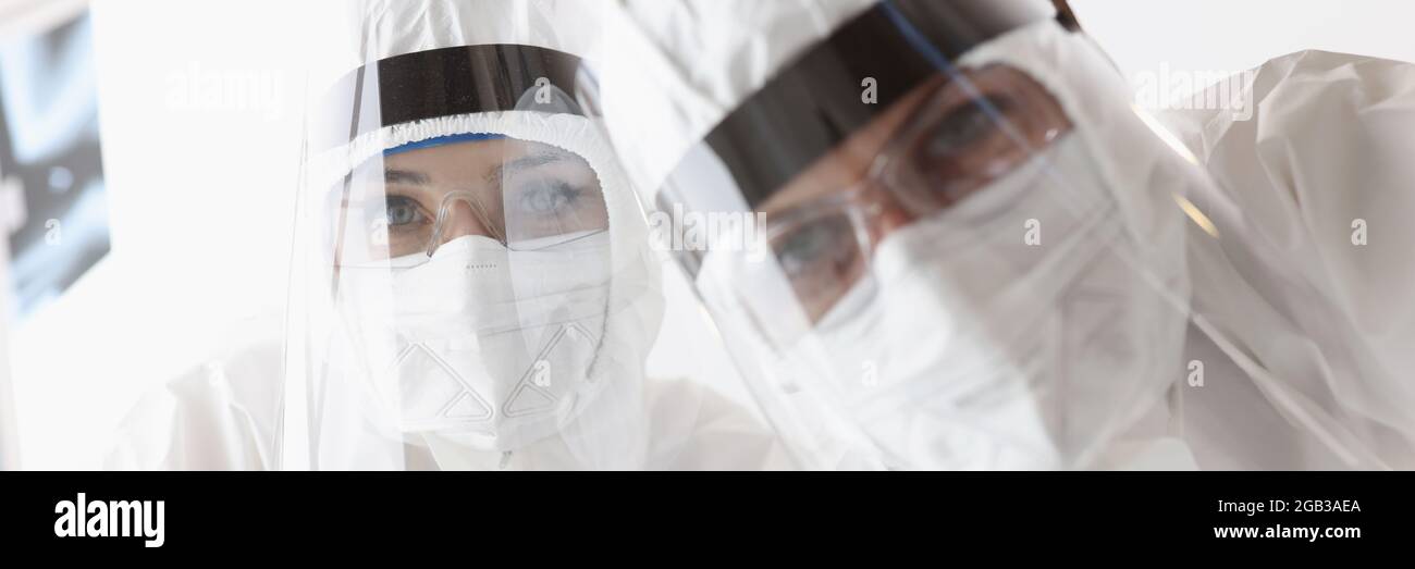 Médicos en trajes protectores antipeste y pantallas mirando al paciente Foto de stock