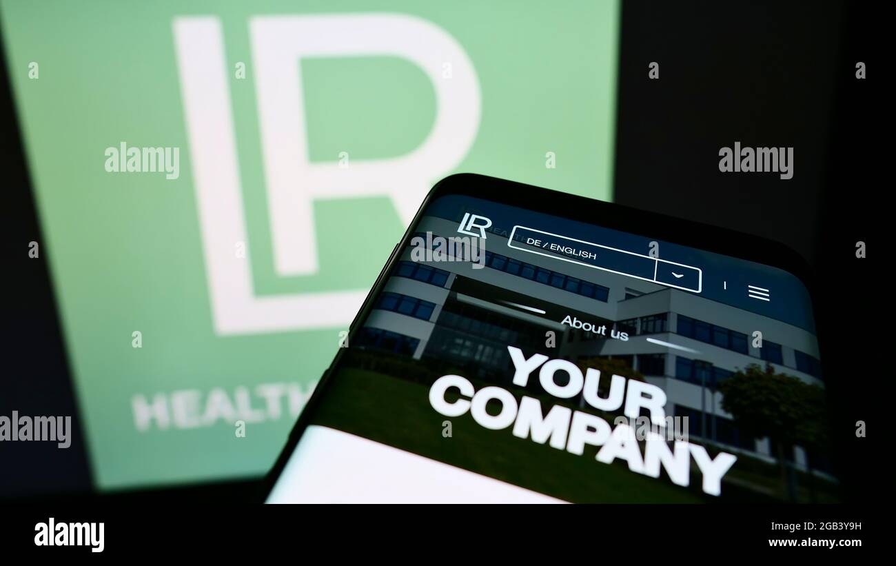 Teléfono móvil con sitio web de la empresa de cosméticos LR Health and Beauty Systems GmbH en pantalla frente al logotipo. Enfoque en la parte superior izquierda de la pantalla del teléfono. Foto de stock