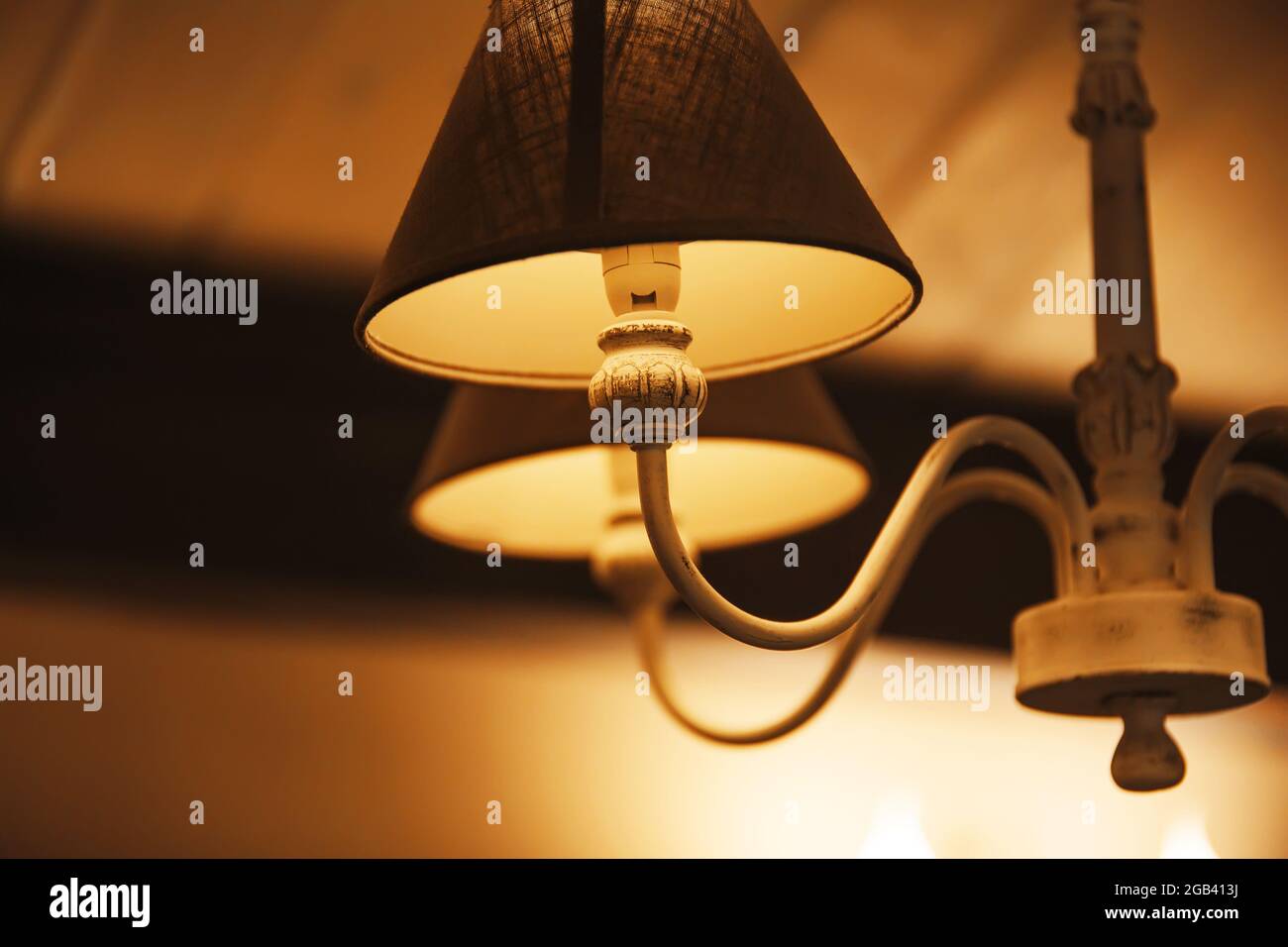Una hermosa y elegante lámpara de araña con cortinas de tela cuelga en la habitación y brilla con luz cálida por la noche, creando un ambiente acogedor. Un motel. Foto de stock