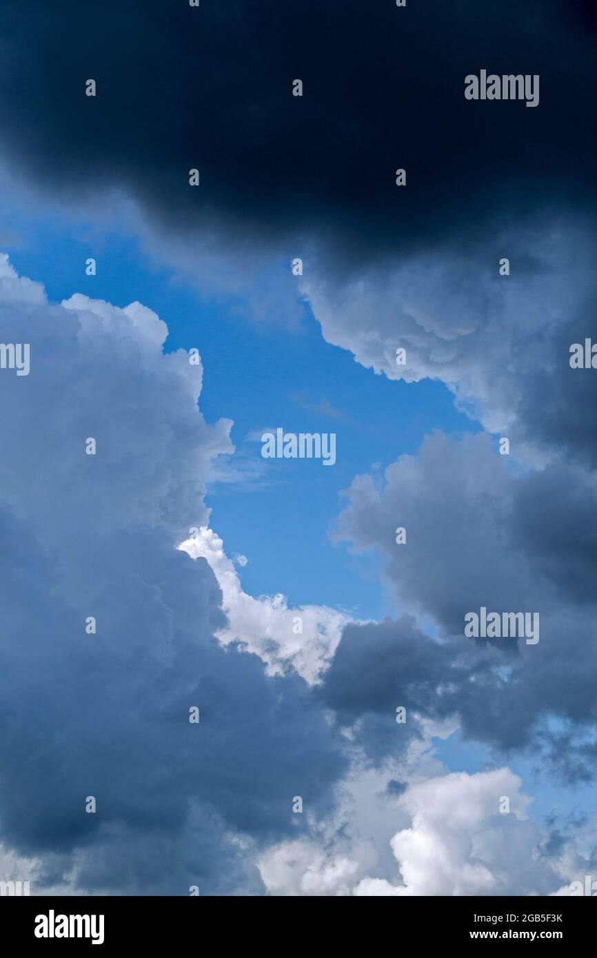 Hueco en nubes cumulus blancas y grises mostrando parche de cielo azul en un día lluvioso en verano Foto de stock