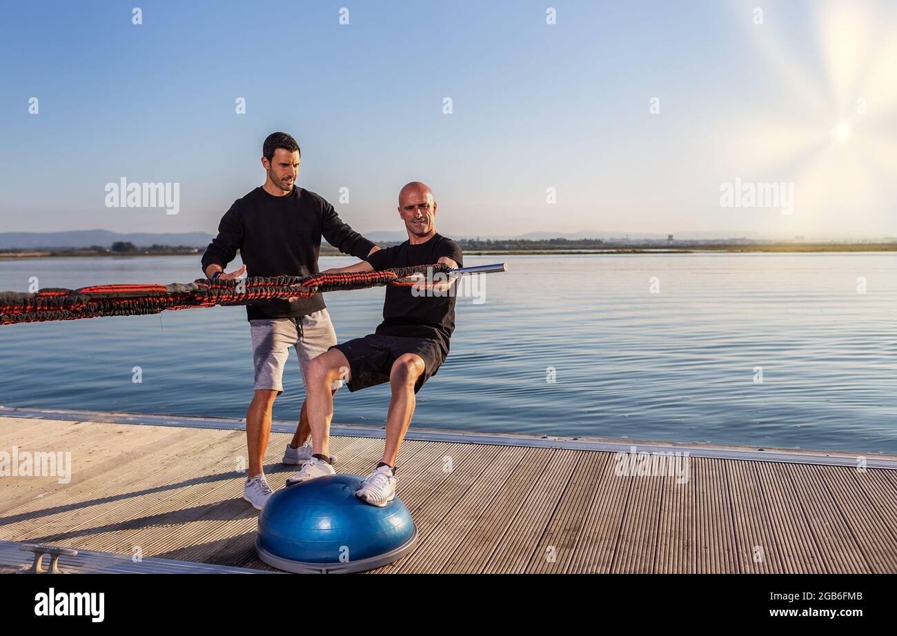 Un windsurfer en una bola de estabilización estimula el montar en una tabla con expansores de caucho. Desarrollar el equilibrio y la estabilidad. Día soleado Foto de stock