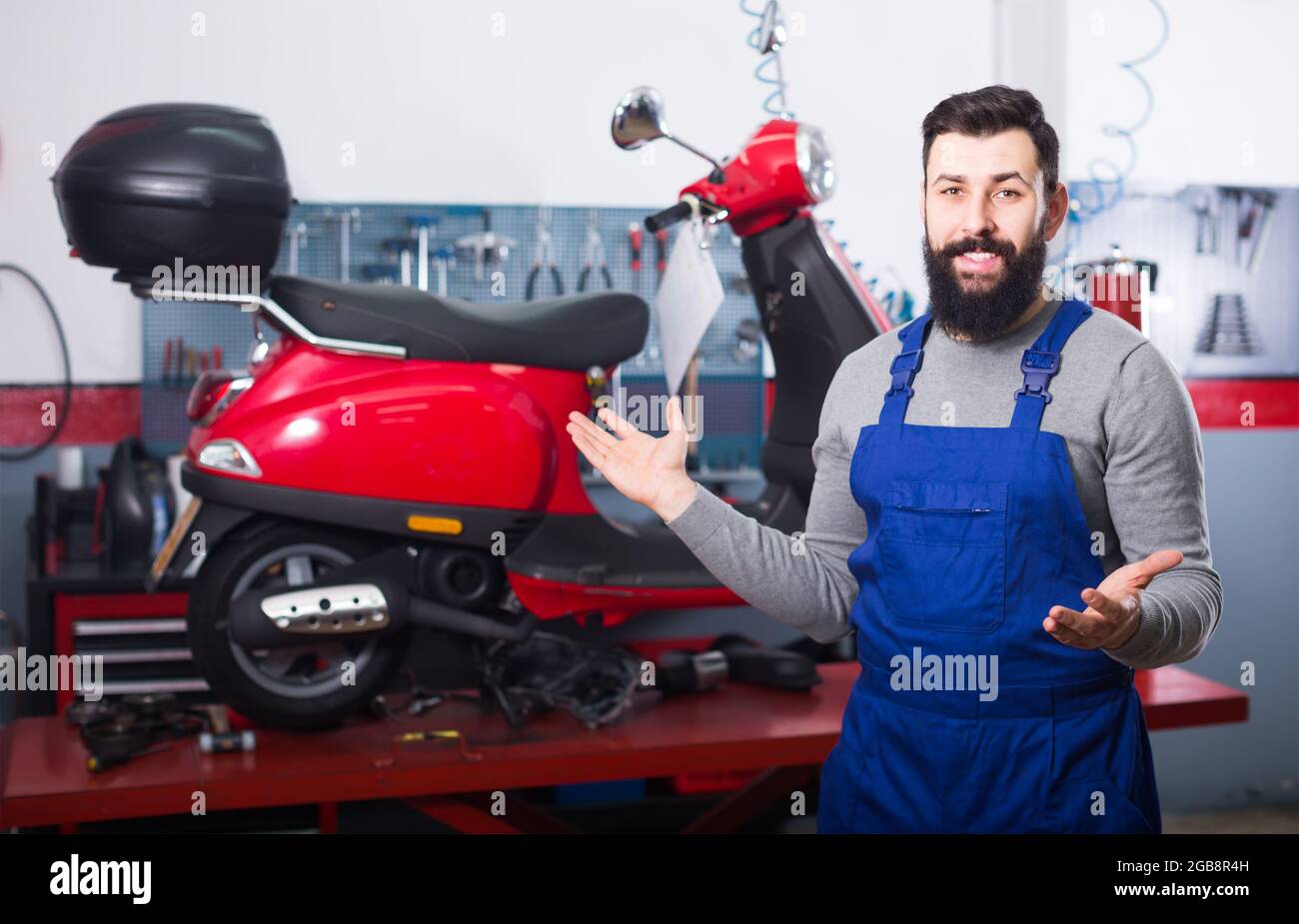 hombre trabajador sonriente mostrando su lugar de trabajo en un taller de motocicletas Foto de stock