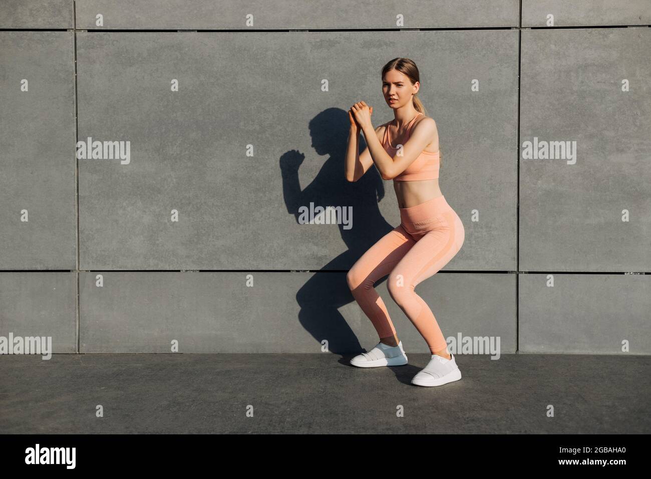 Vista lateral foto de la mujer joven en forma que hace sentadas, ejercicio  en las nalgas al aire libre, entrenamiento en el fondo de la pared de  hormigón urbano, fitness mujer ejercicio