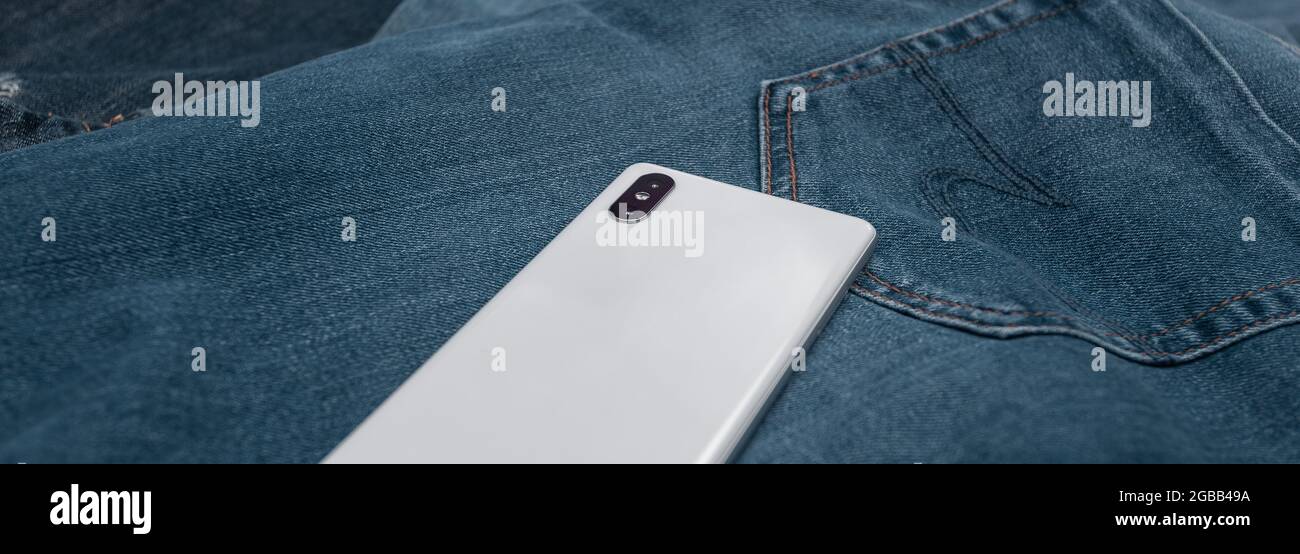 teléfono móvil panorámico blanco sobre jeans azules Foto de stock