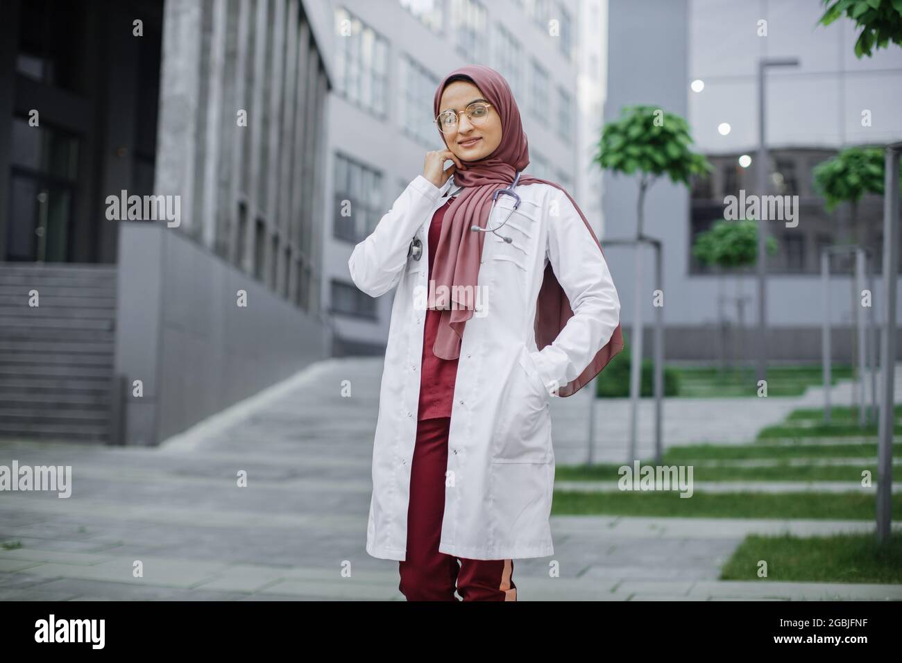 Retrato al aire libre de la hermosa enfermera musulmana malaya con  estetoscopio. Doctora mujer árabe segura en el pañuelo tradicional de pie  fuera de la clínica moderna o los edificios del hospital