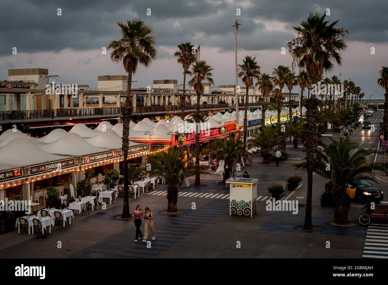 Dos mujeres caminan por las terrazas casi vacías de los bares y  restaurantes del Port Olimpic de Barcelona después de un día tormentoso en  la ciudad Fotografía de stock - Alamy