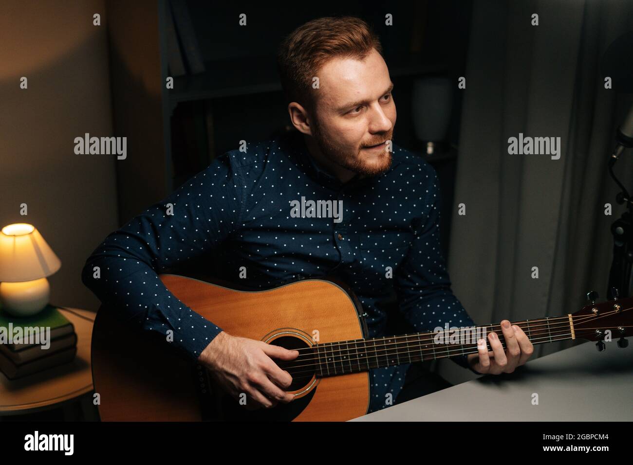 Retrato de medio disparo del cantante guitarrista hombre cantando  emocionalmente en el micrófono de condensador y tocando la guitarra  acústica en el oscuro estudio de grabación en casa Fotografía de stock -