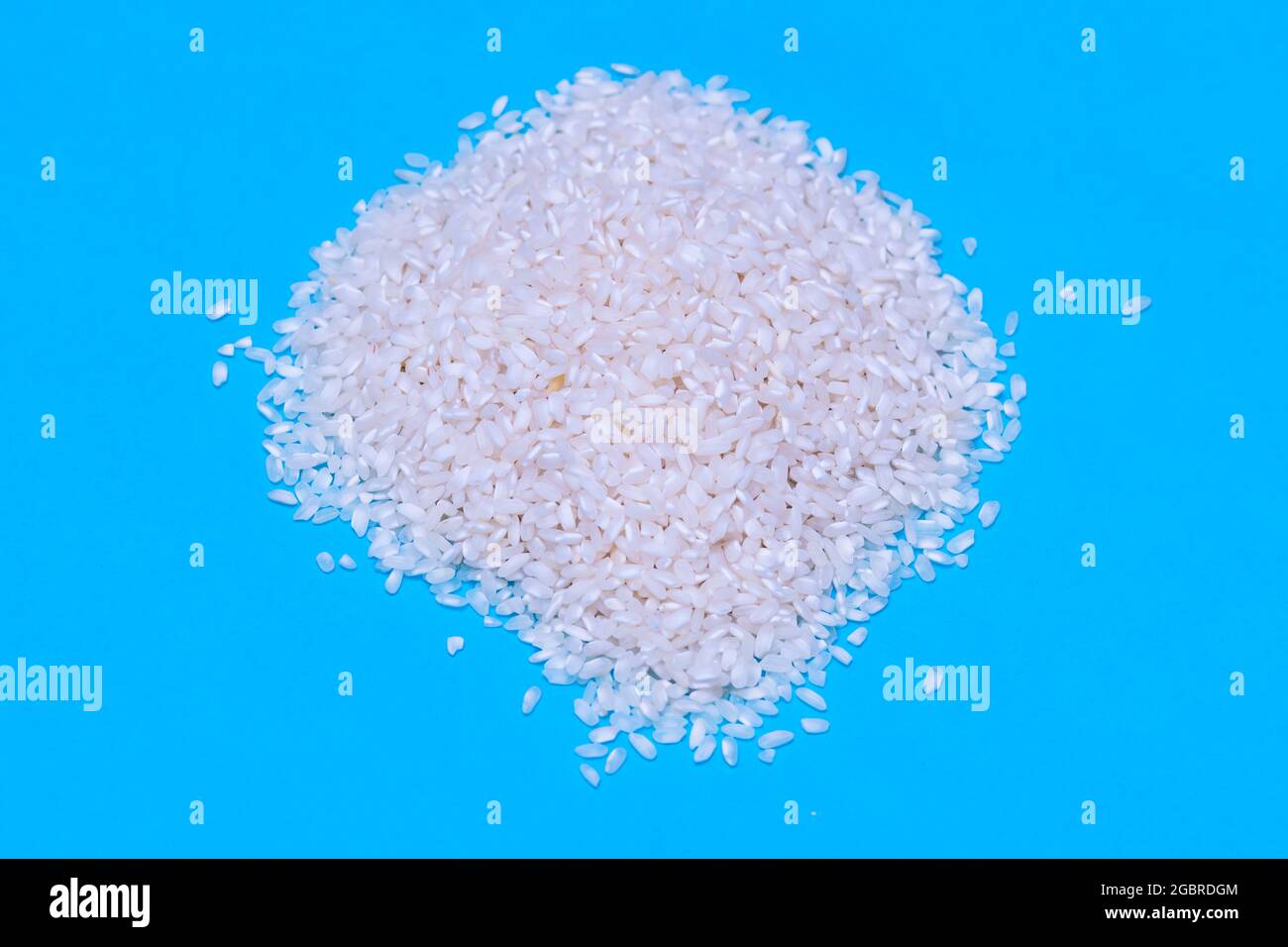 un puñado de arroz blanco sin cocinar sobre fondo azul. concepto de comida, cocina y vida saludable Foto de stock