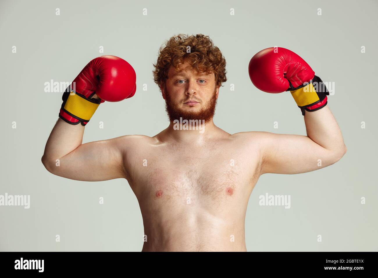 Divertido hombre de cabeza roja en pantalones cortos de boxeo azul y  guantes aislados sobre fondo de estudio gris. Concepto de deporte, humor y  cuerpo positivo Fotografía de stock - Alamy