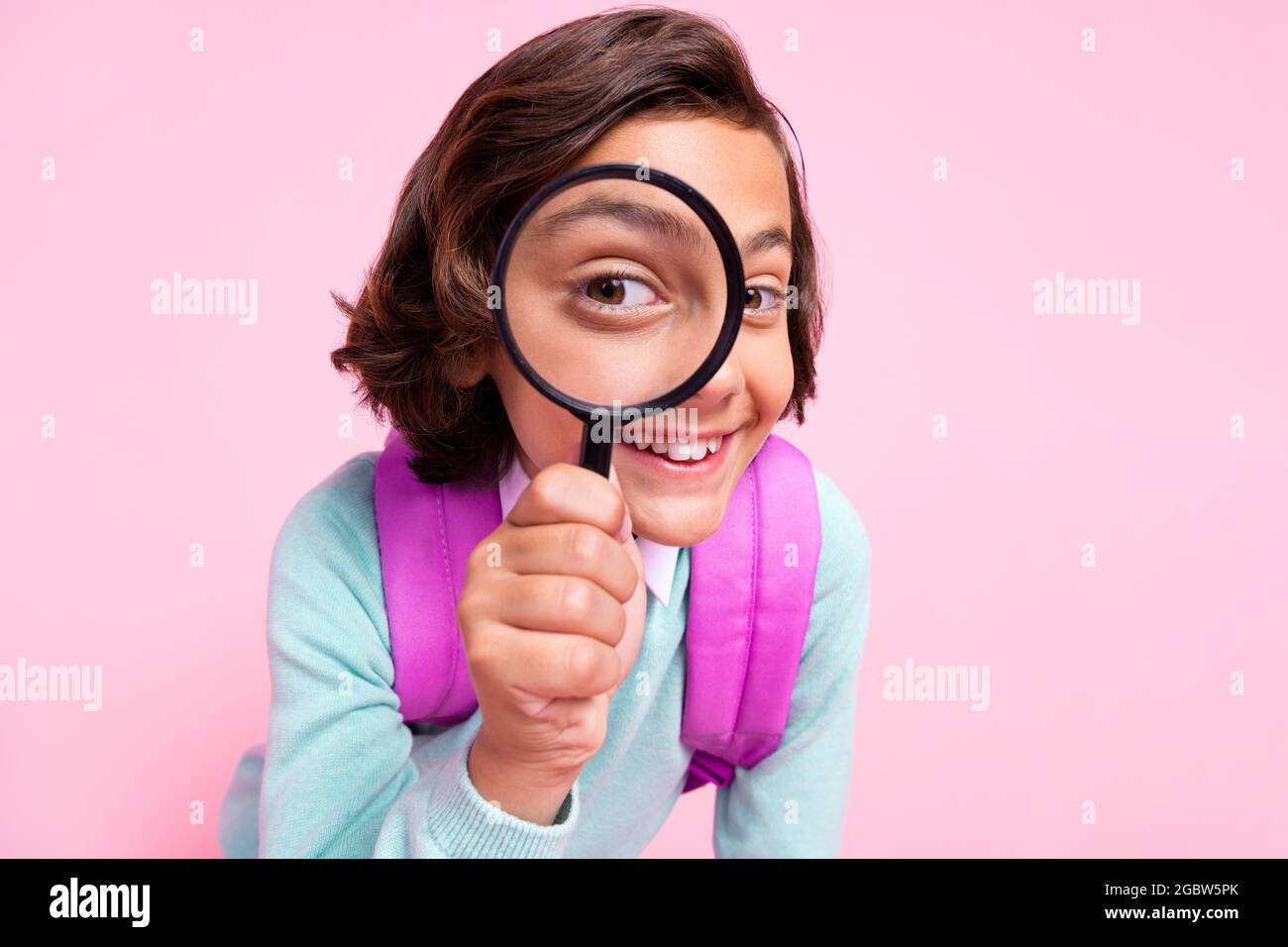 Foto de chico detective alegre sostener loupe mirar ver ampliar ojo bolsa ropa de ojos camisa de color rosa aislado fondo Foto de stock