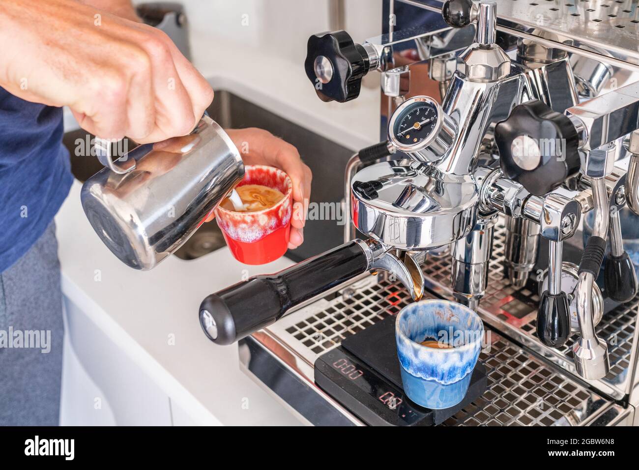 Hombre barista que hace el cortado en la máquina de café que vierte la  leche en la taza del espresso en la cafetería. Casa por la mañana tomar el  desayuno en la