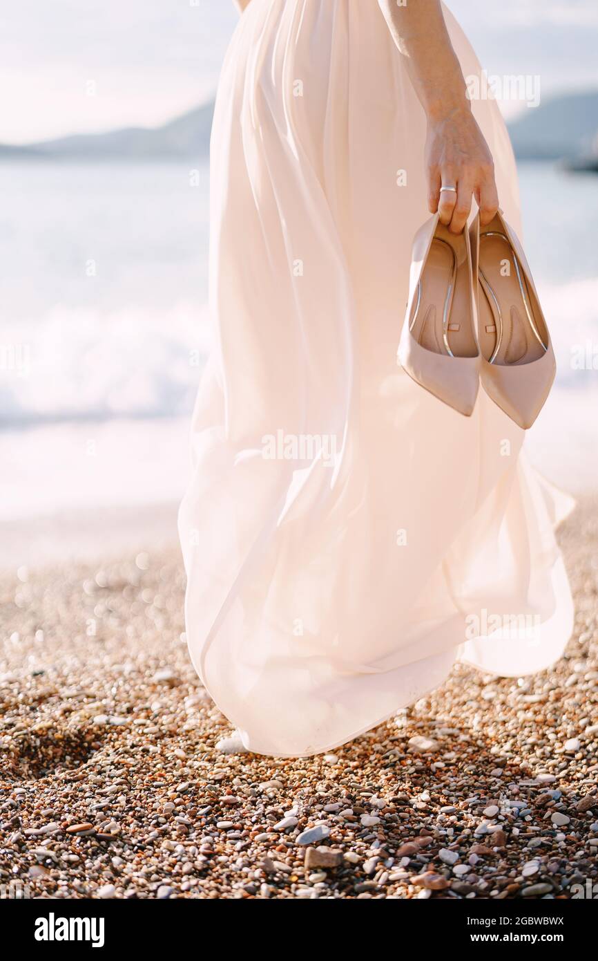 Novia con zapatos de tacón alto en su mano camina a lo largo de la playa.  Primer plano Fotografía de stock - Alamy