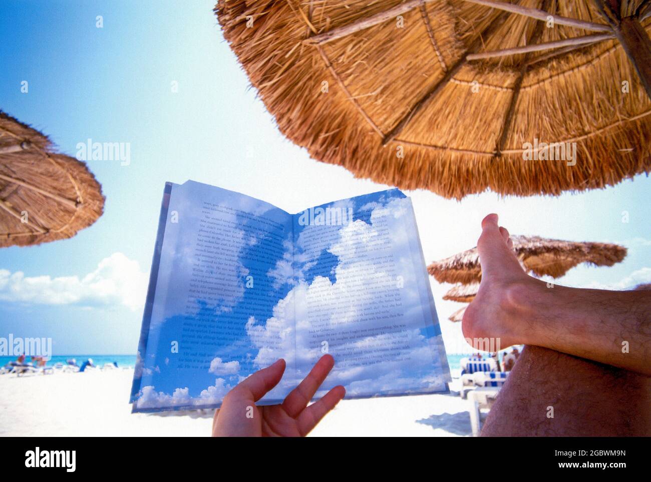 Vacaciones y relajación, persona leyendo un libro en una playa bajo una palapa, concepto de imagen con nubes superpuestas sobre el texto para soñar lejos Foto de stock