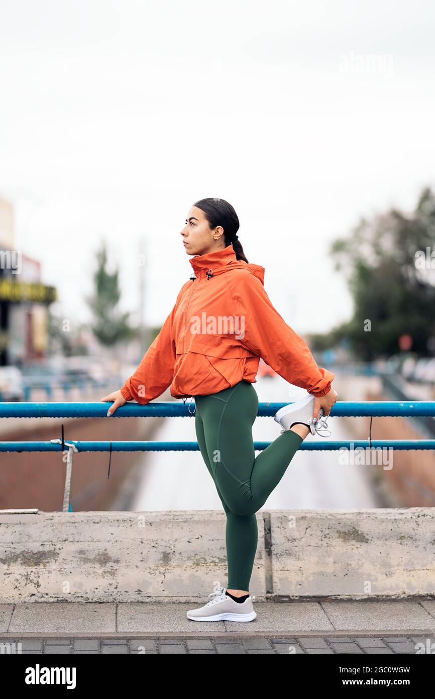 Joven mujer activa que usa ropa deportiva mirando al frente y estirándose  después de correr en la ciudad durante el día lluvioso Fotografía de stock  - Alamy