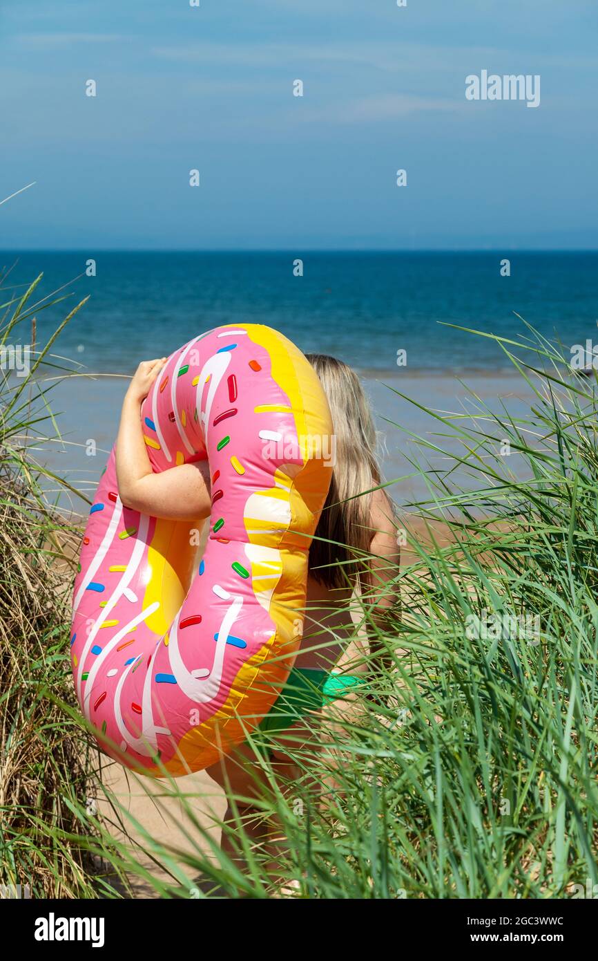 Una mujer joven con un donut inflable que se dirige a la playa de Gullane, East Lothian, Escocia Foto de stock