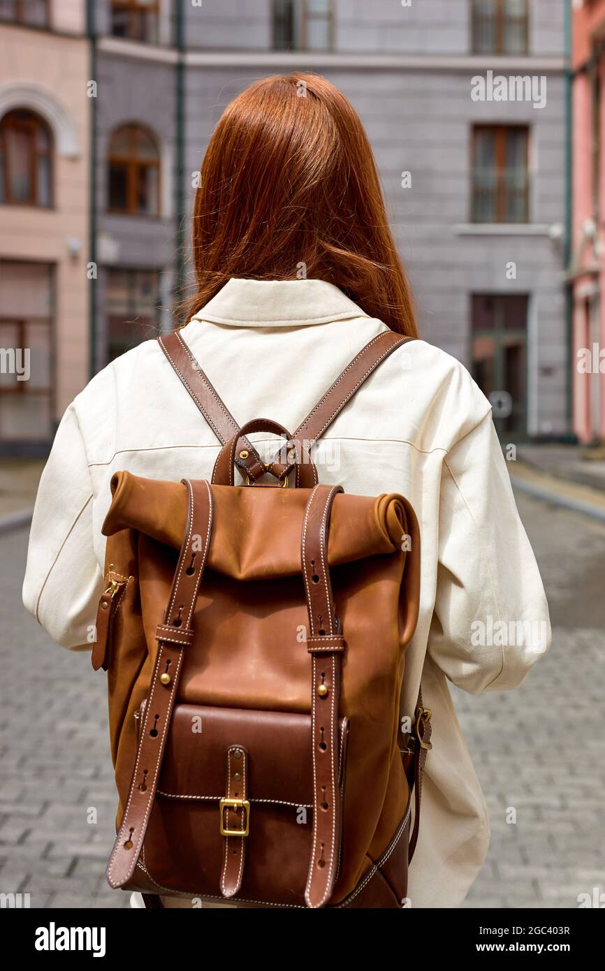 Mujer joven de pelirroja con mochila de cuero, concepto viaje. Vista de la parte trasera de la mujer viajera turista caminando solo por la ciudad. Vista desde atrás en unrec