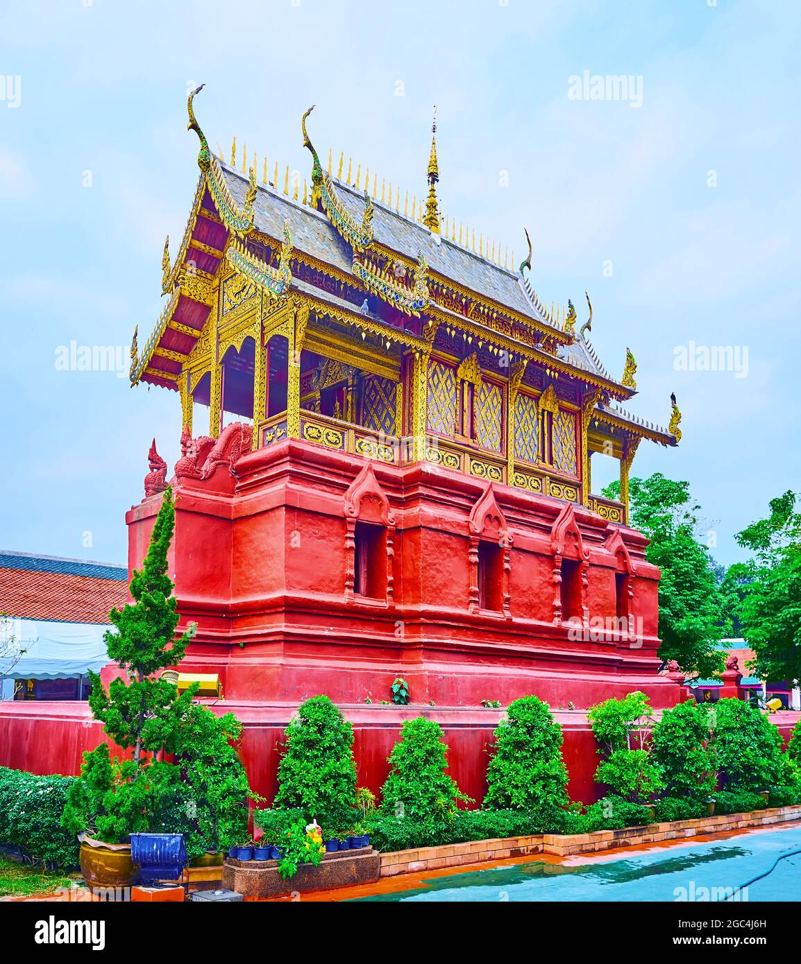 El edificio rojo brillante de la biblioteca budista de Ho Trai con techo de piathe (hastial) y decoraciones talladas ornamentadas, Wat Phra That Hariphunchai Temple, Lamphun, Th Foto de stock