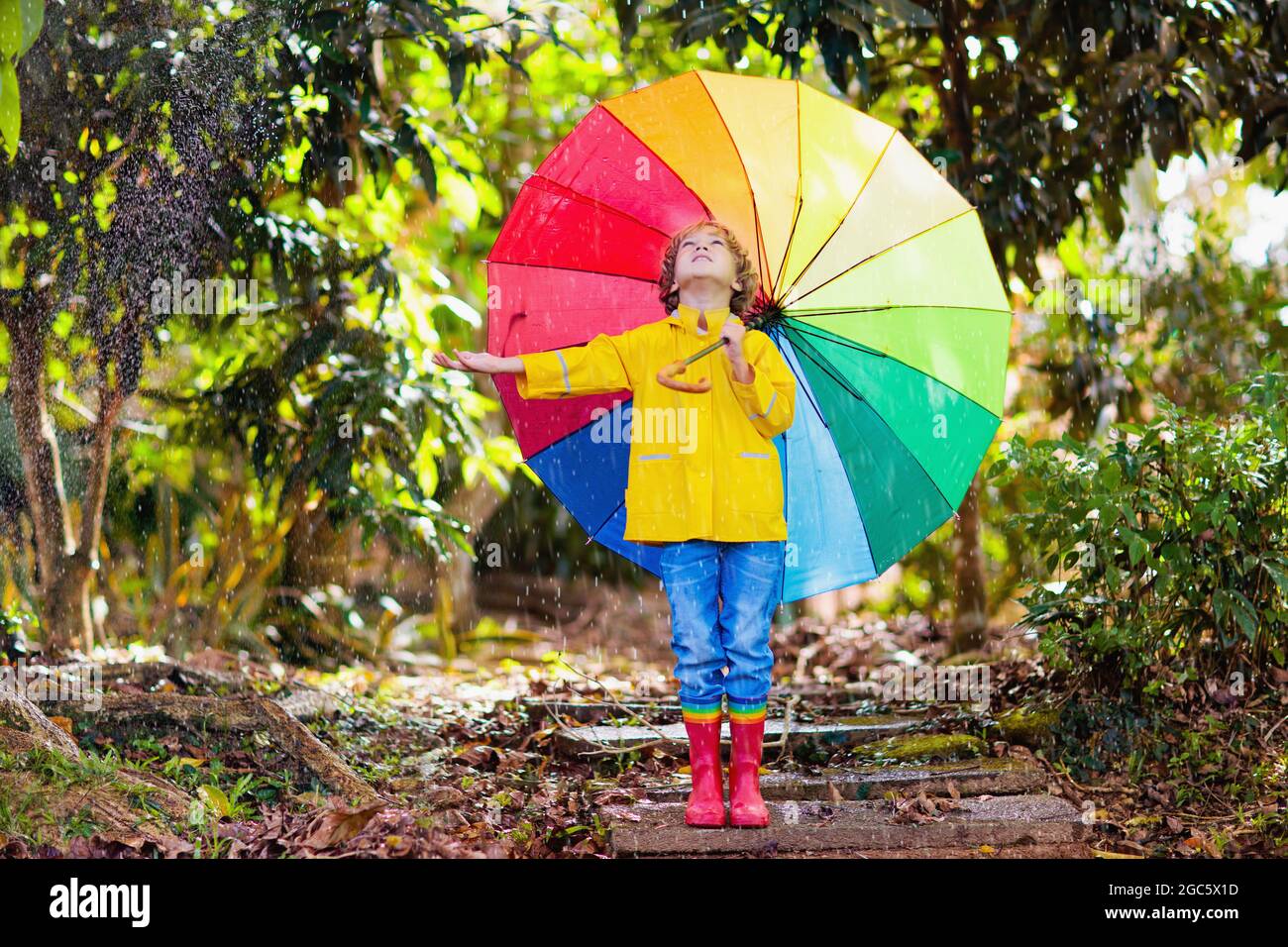 Niños jugando bajo la lluvia de otoño. Niño con paraguas. Niño corriendo en  la calle de la ciudad en la temporada de otoño. Diversión al aire libre  para los niños en cualquier