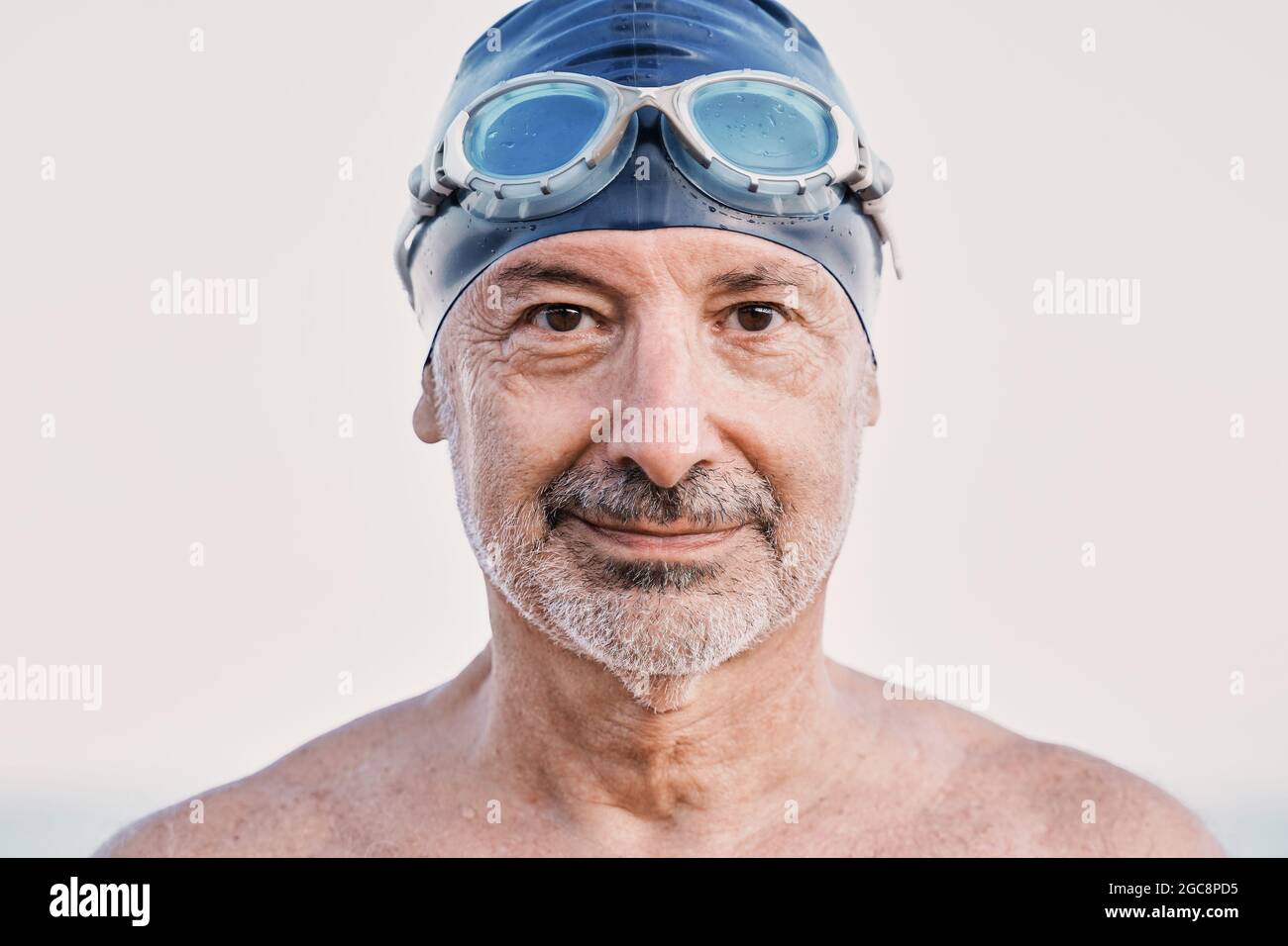 Nadador hombre mayor mirando la cámara antes de entrenar al aire libre en la playa - concepto de competición deportiva de agua abierta Foto de stock