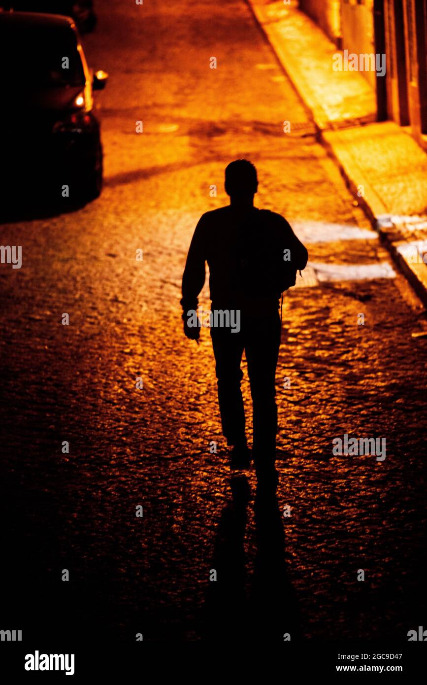 Vista trasera de un hombre caminando solo por la noche en un callejón de  adoquines Fotografía de stock - Alamy