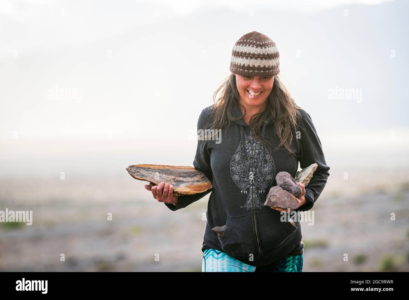 Mujer recogiendo rocas en tierra pública en el desierto de roca negra con coloridas leggings Foto de stock