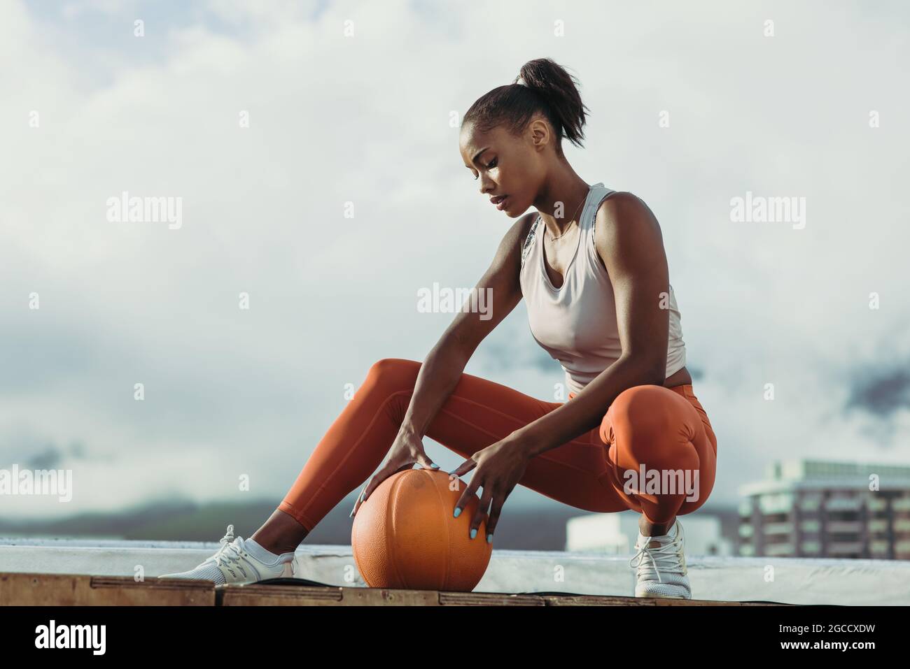 Deportista con baloncesto sentado en la azotea. Fitness mujer relajarse después de una sesión de ejercicio al aire libre. Foto de stock